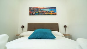 A hotel room with a bed, a painting of a cityscape, and two bedside lamps.