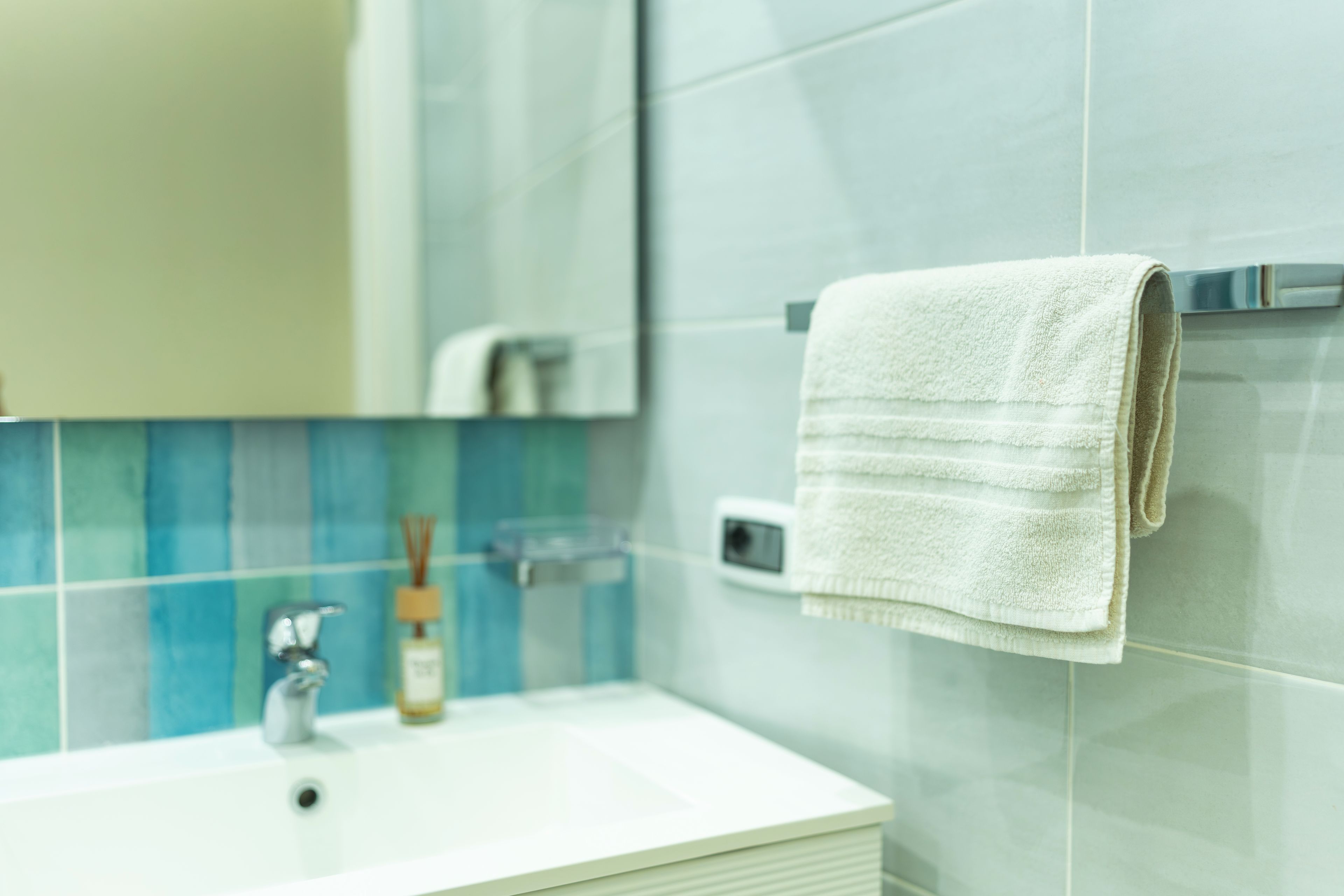 A bathroom with a white sink, a mirror, and a towel hanging on a towel rack.