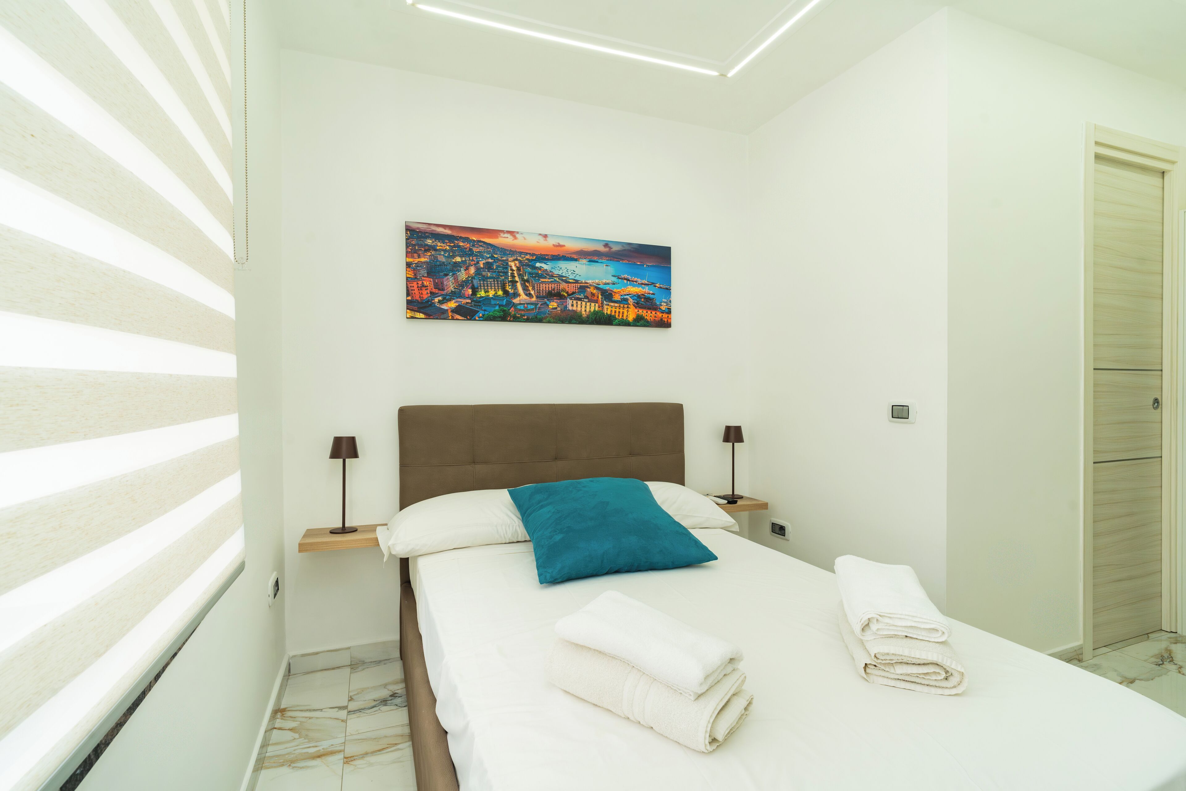 A hotel room with a bed, a nightstand, a lamp, a painting, and a door.