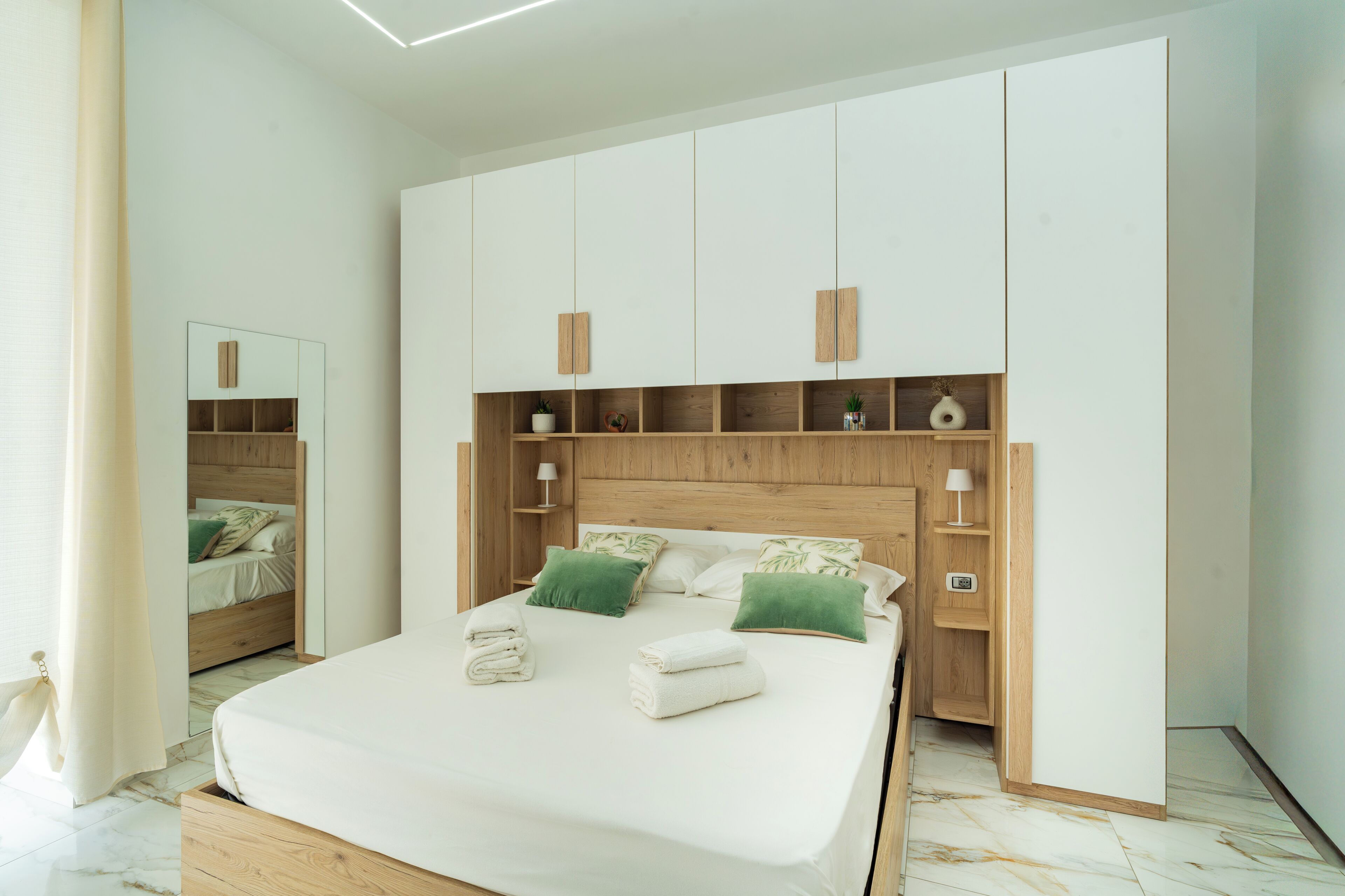 Ein Schlafzimmer mit einem großen Bett, einem Holzkopfteil, integrierten Regalen und einem Spiegel.