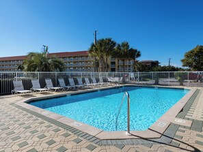 A swimming pool with lounge chairs, a tiled deck, and a building with balconies in the background. - Wonderful Pet Friendly Condo Close to Beach! (Miramar Beach)