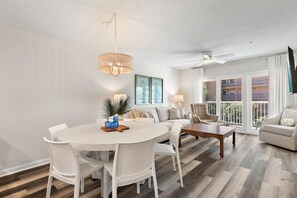 A modern living room with a dining area, a ceiling fan, and a view of the outdoors. - Wonderful Pet Friendly Condo Close to Beach! (Miramar Beach)