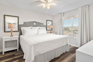 Ein ordentlich eingerichtetes Schlafzimmer mit einem Bett, Nachttischen, einem Deckenventilator und einem Fenster mit Jalousien.