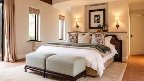 A bedroom with a large bed, a bench, two wall-mounted lamps, and a framed picture on the wall. - Avianto Pty Ltd (Muldersdrift)