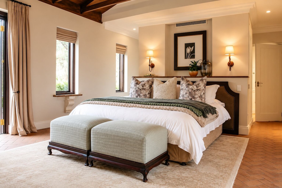 A bedroom with a large bed, a bench, two wall-mounted lamps, and a framed picture on the wall.