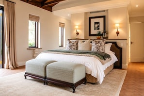 A bedroom with a large bed, a bench, two wall-mounted lamps, and a framed picture on the wall. - Avianto Pty Ltd (Muldersdrift)