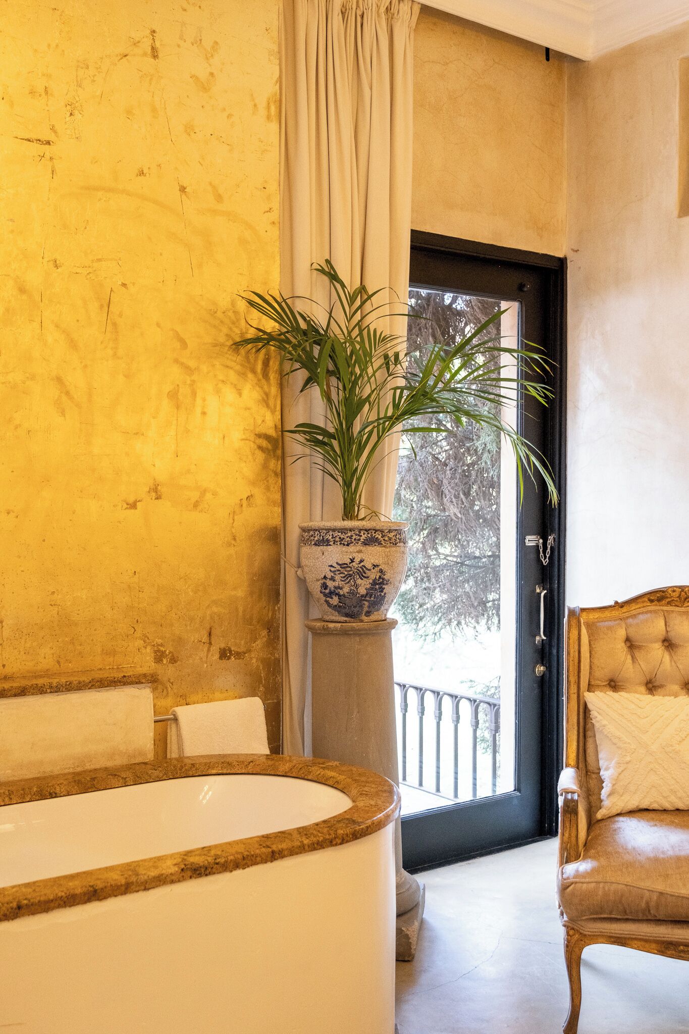 A bathroom with a bathtub, a potted plant, and a chair.