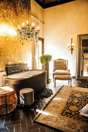 A luxurious bathroom with a freestanding bathtub, a classic chair, and a chandelier. - Avianto Pty Ltd (Muldersdrift)