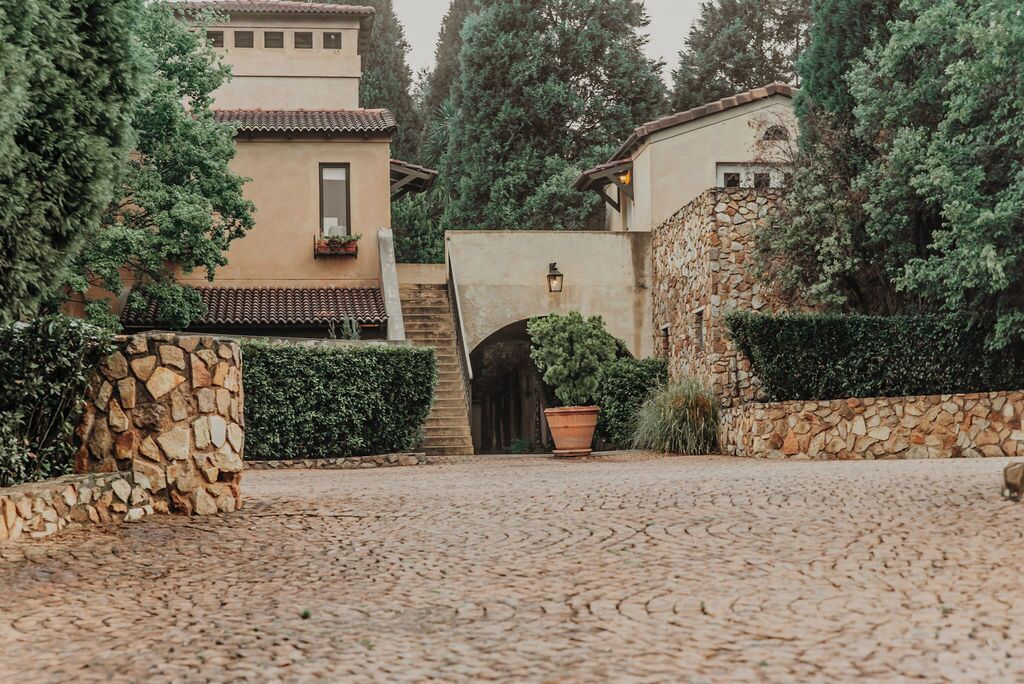 A courtyard with cobblestone flooring, stone walls, and a central archway.