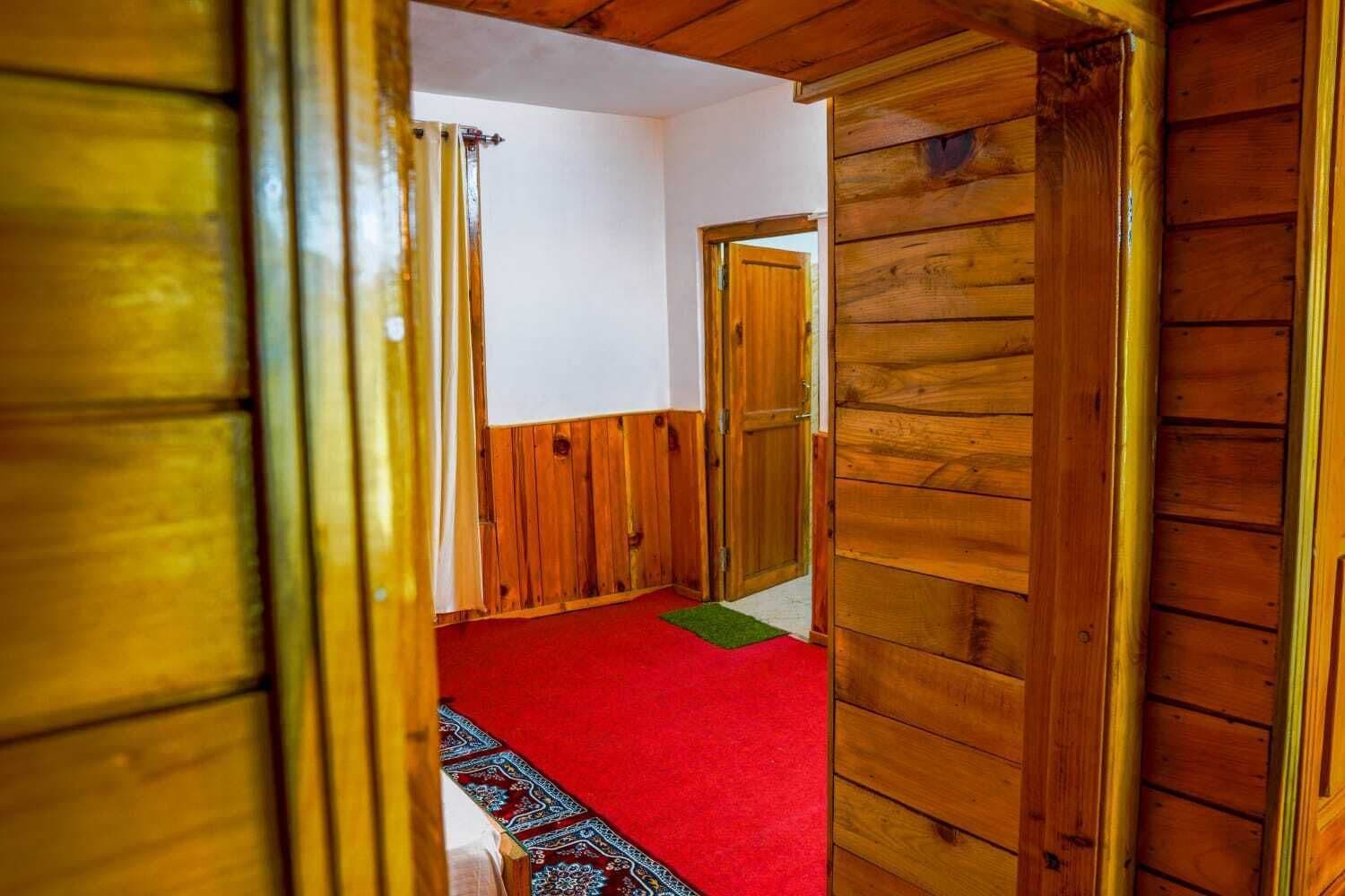 A wooden interior hallway with a red carpet, wooden doors, and a patterned rug.