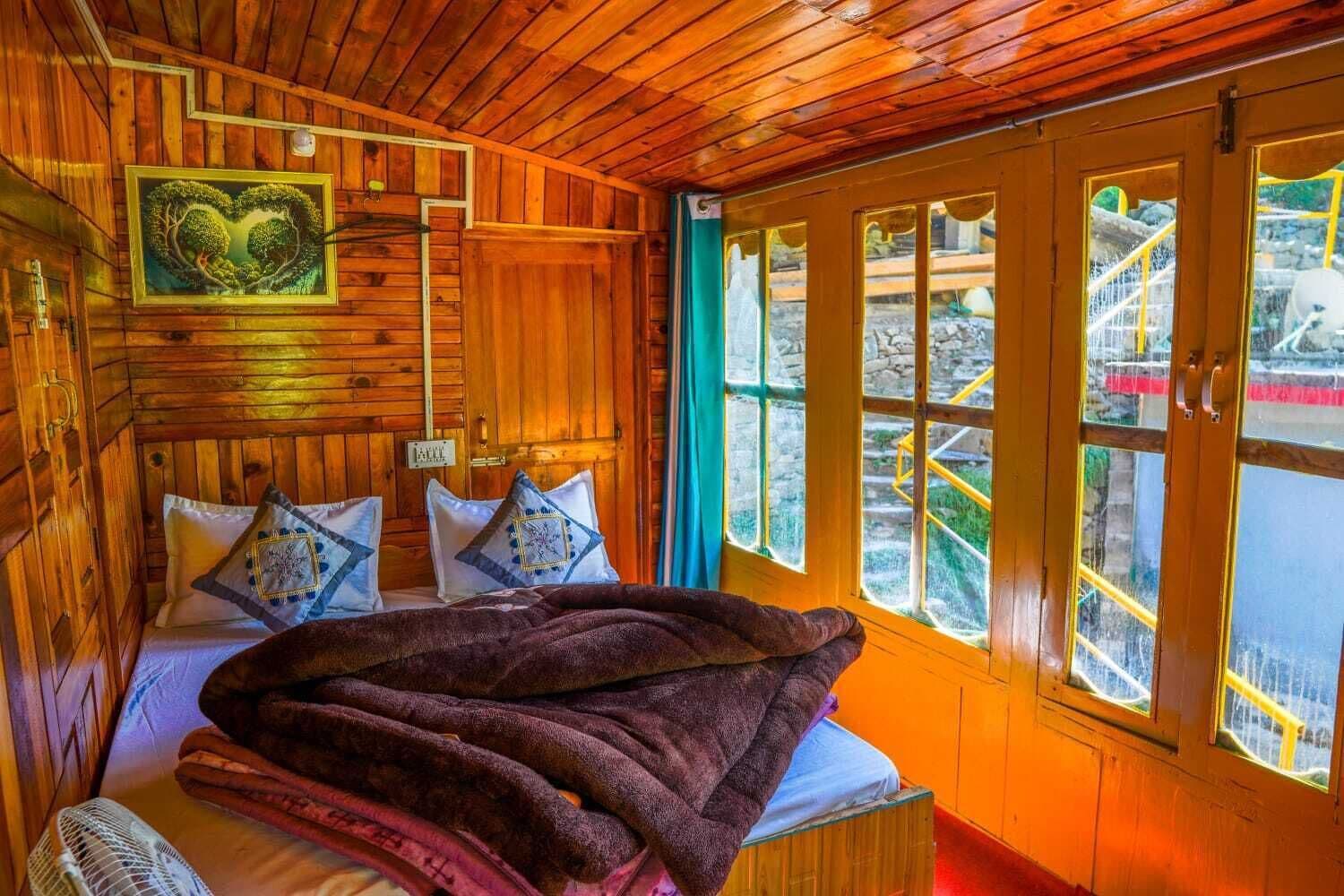 Habitación de cabaña de madera con cama, almohadas, una colcha y ventana con vista a una estructura de piedra.