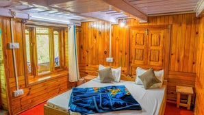 A wooden cabin room with a bed, a window with curtains, and a small table. - Neervan Resort (Gushaini)