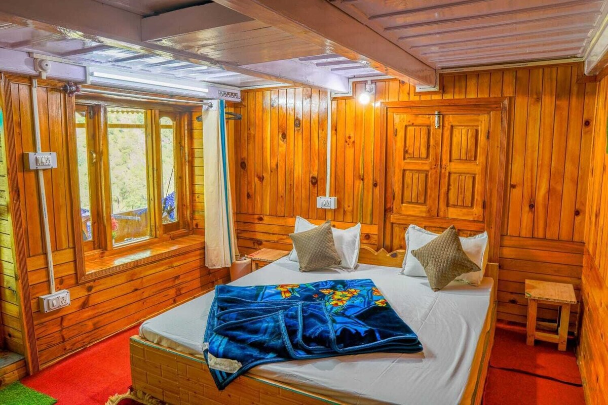 A wooden cabin room with a bed, a window with curtains, and a small table.
