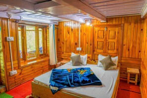 A wooden cabin room with a bed, a window with curtains, and a small table. - Neervan Resort (Gushaini)
