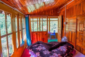 A wooden cabin room with a bed, a chair, and a fan. - Neervan Resort (Banjar)