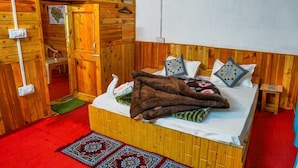A wooden room with a bed, a small table, and a red carpet. - Neervan Resort (Gushaini)