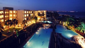 Un hôtel doté de plusieurs piscines, offrant une vue sur la plage et dont l’extérieur est bien éclairé.