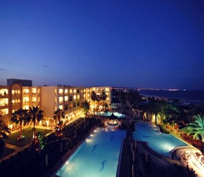 A hotel with multiple swimming pools, a beachfront view, and a well-lit exterior. - Paradis Palace (Hammamet Sud)