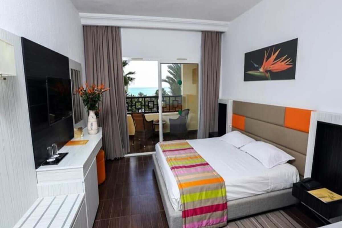A hotel room with a bed, a TV, a desk, and a view of the outside.