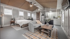 A compact bedroom with a bed, a sofa, a coffee table, and a kitchen area with a refrigerator and a microwave. - The Cozy Cottage - Private Yard • Pet Friendly • Seminole Heights (Tampa)