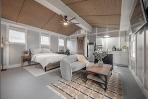 A compact bedroom with a bed, a sofa, a coffee table, and a kitchen area with a refrigerator and a microwave.