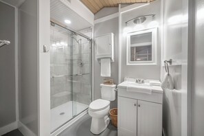 A bathroom with a glass-enclosed shower, a toilet, a sink with a mirror, and a towel rack.