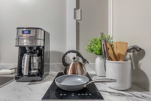 A kitchen with a coffee maker, kettle, frying pan, and utensils on a countertop.