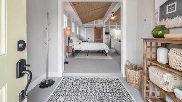 A hallway leading to a bedroom with a bed, bedside table, and a floor lamp. - The Cozy Cottage - Private Yard • Pet Friendly • Seminole Heights (Tampa)
