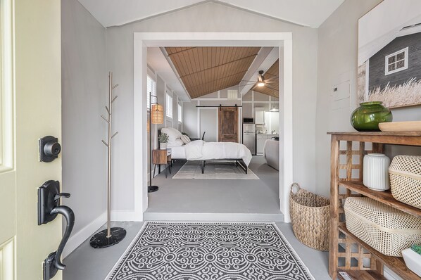 A hallway leading to a bedroom with a bed, bedside table, and a floor lamp.