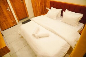Habitación de hotel con cama doble, dos almohadas, una toalla enrollada, suelo de madera y una puerta de madera.