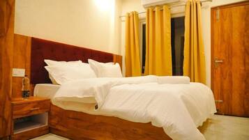 Une chambre d’hôtel avec une tête de lit en bois, un lit avec une literie blanche, une table de chevet avec une bouteille, et une porte avec un cadre en bois.