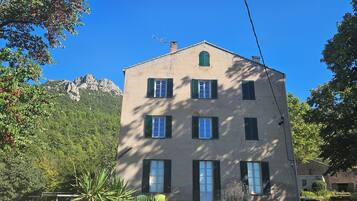 A multi-story building with a symmetrical facade, multiple windows with shutters, and a chimney.