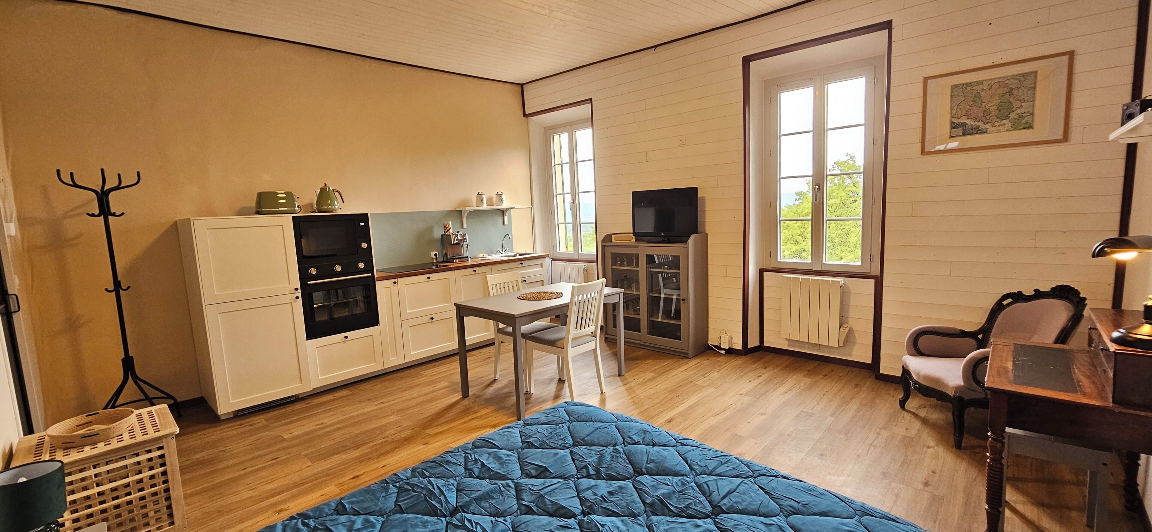 Een kleine kamer met een kitchenette, een eethoek en een bed.