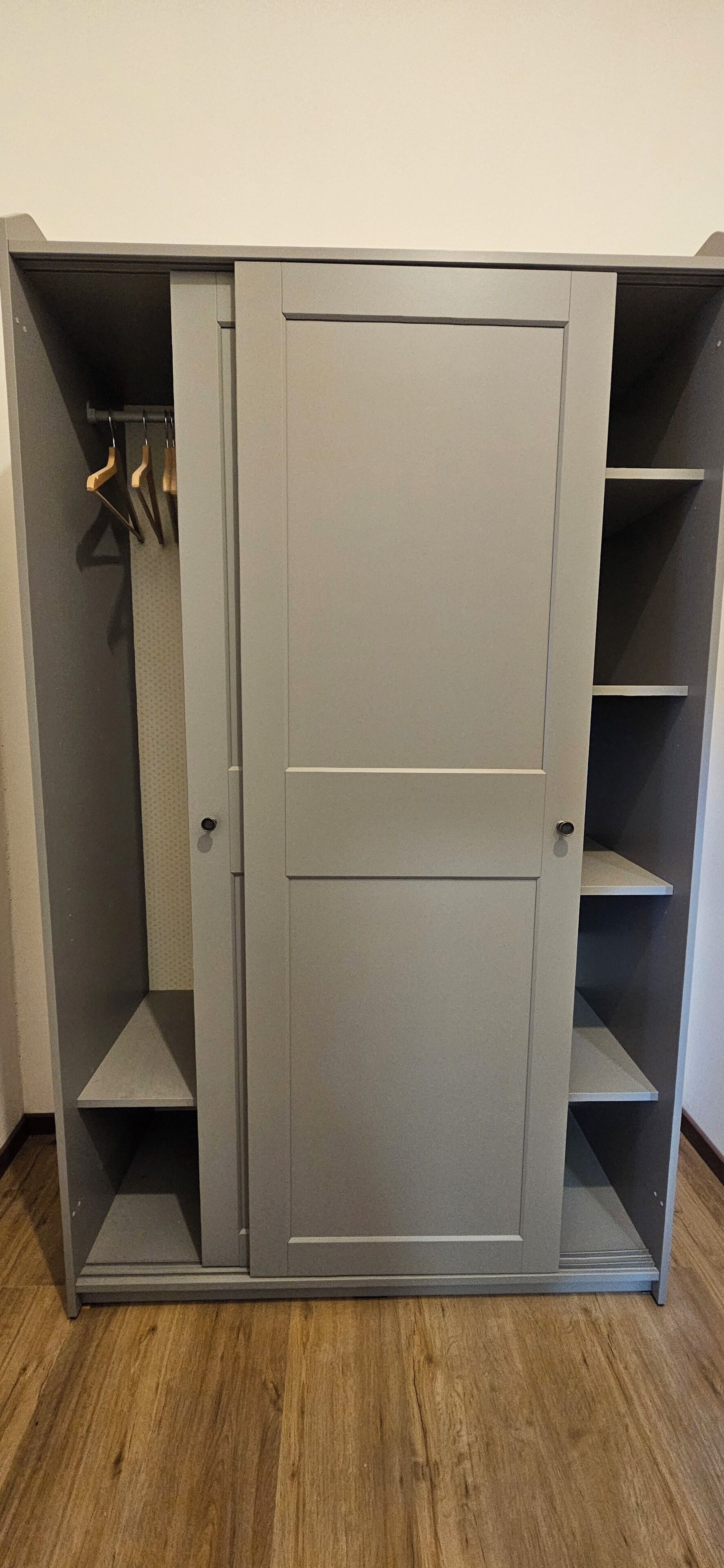 A grey wardrobe with a door, two shelves, and a hanging rod.