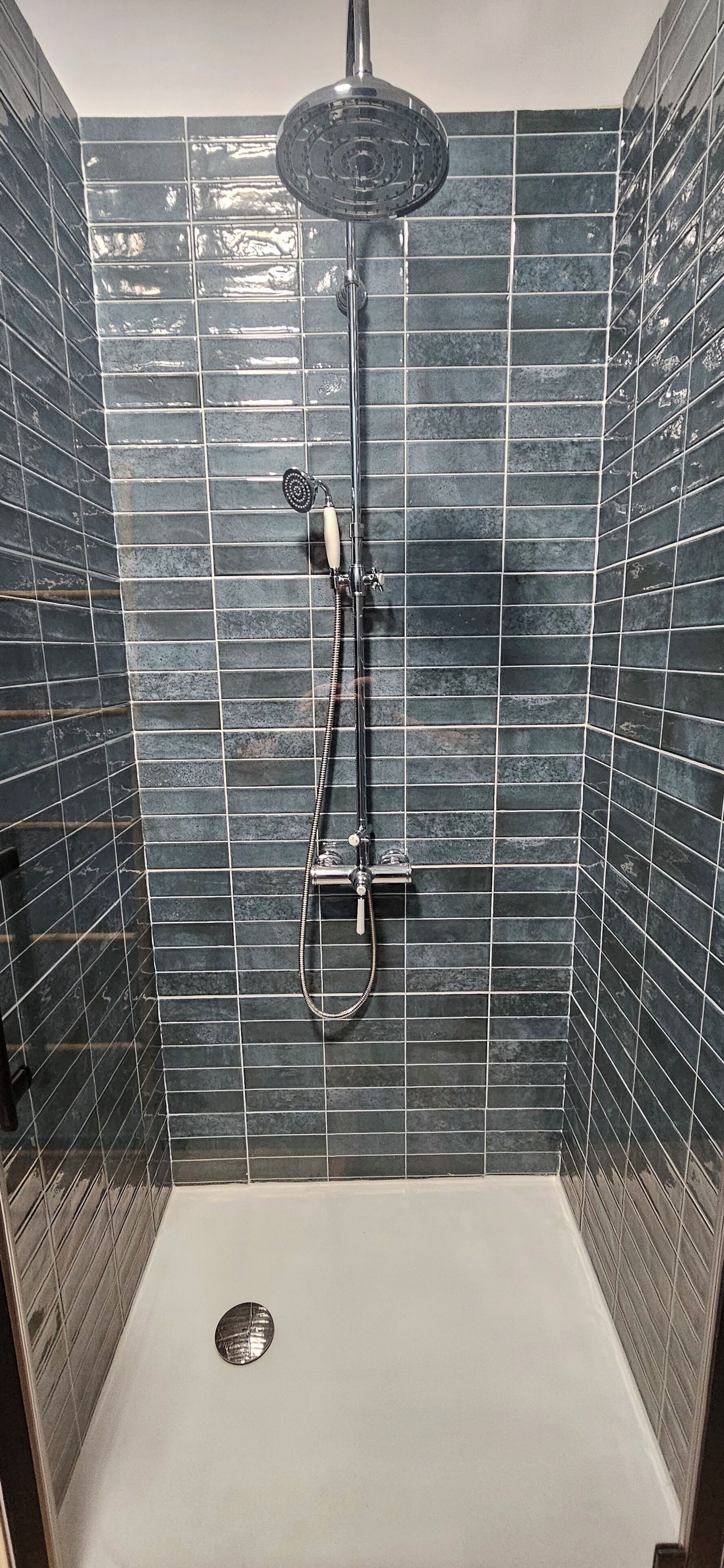 A shower with a handheld showerhead and a wall-mounted rain showerhead, set against a tiled wall.