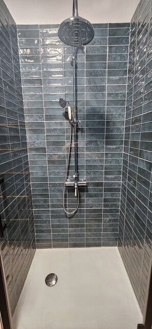Chuveiro com chuveiro manual e ducha de teto, em frente a uma parede revestida com azulejos.