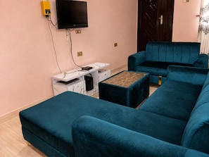 Ein Wohnzimmer mit einem türkisfarbenen Sofa, einem Couchtisch und einem an der Wand befestigten Fernseher.