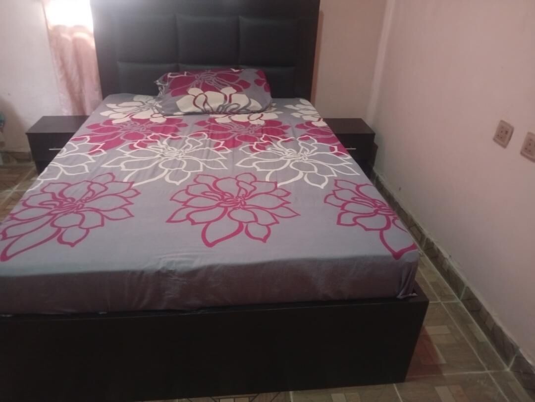 Een bed met een bloemenprint deken, hoofdbord en nachtkastje met lamp.
