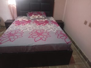 A bed with a floral bedspread, a headboard, and a nightstand with a lamp.