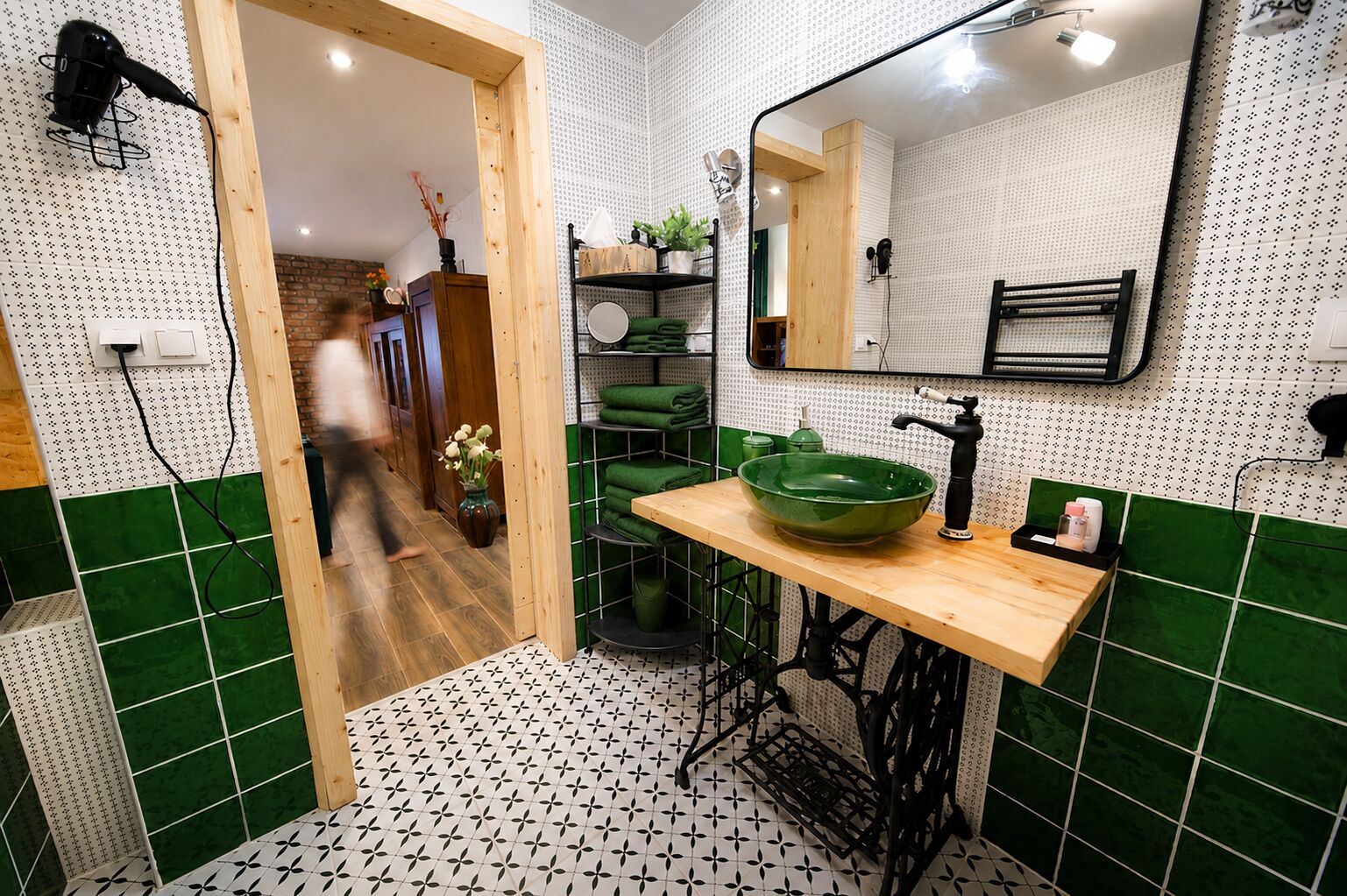 Ein Badezimmer mit grün-weiß gefliestem Boden, einem hölzernen Waschtisch mit einem grünen Becken und einem Spiegel über dem Waschbecken.
