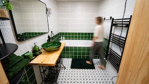 Ett badrum med ett grönt och vitt kaklat golv, ett handfat i trä med en grön tvättskål och en svart handdukshängare.