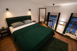 Ein Schlafzimmer mit einem großen Bett, Nachttischen, einem Spiegel, einem Fenster mit Vorhängen und Blick ins Freie.