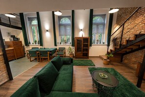 A modern living room with a green sofa, dining table, and chairs, a staircase, and large windows with curtains. - Cozy loft bedroom apartment in gorgeous Budapest (Budapest)
