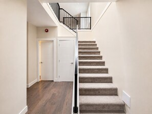 A staircase with carpeted steps and a metal railing, leading to a landing with a door.