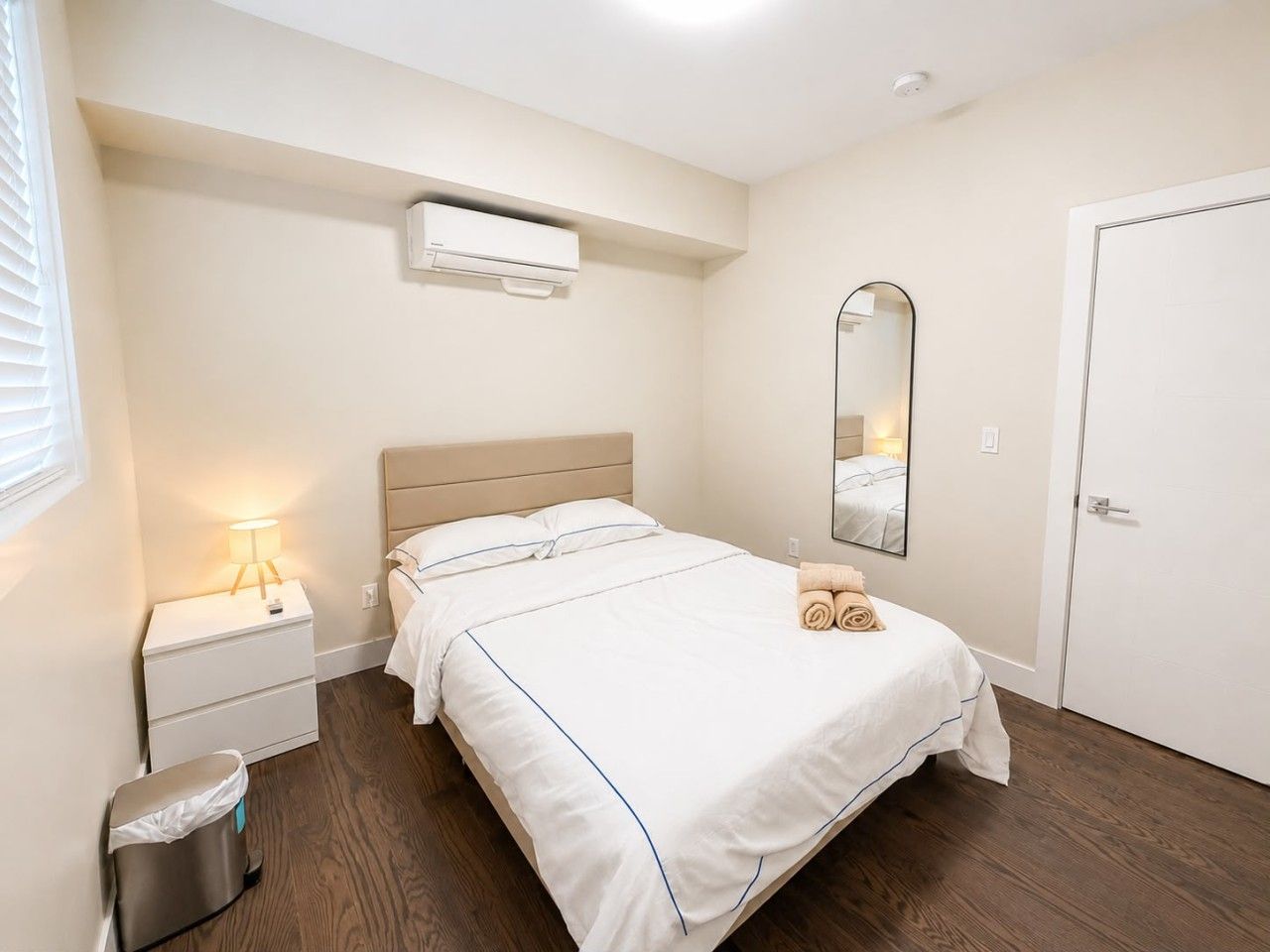 Ein Hotelzimmer mit Bett, Nachttisch, Lampe, Spiegel und einer Tür.