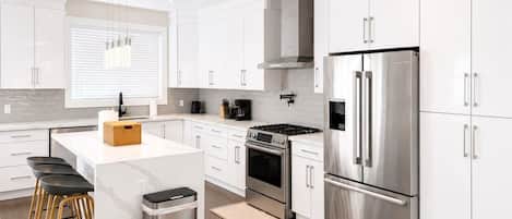 Una cocina moderna con armarios blancos, electrodomésticos de acero inoxidable y una isla central con taburetes.