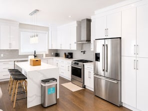 A modern kitchen with white cabinetry, stainless steel appliances, and a central island with stools.