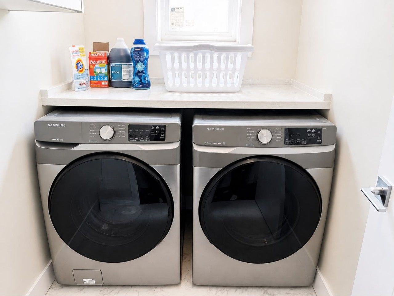 A laundry area with two Samsung washing machines and a basket on the countertop.