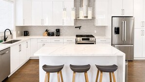 Una cocina moderna con armarios blancos, una isla central con taburetes, electrodomésticos de acero inoxidable y un salpicadero con diseño texturizado.