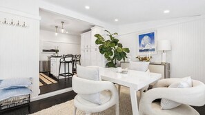 A modern kitchen with white cabinetry, a dining table with chairs, and a large potted plant. - Completely Renovated Sag Harbor Cottage with Lush Gardens, Pergola, and... (Sag Harbor)